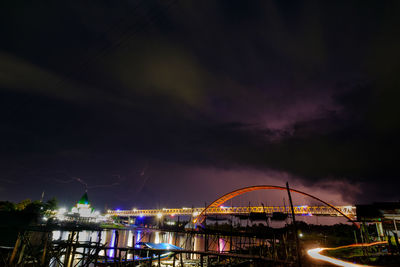 Illuminated bridge over river against cloudy sky