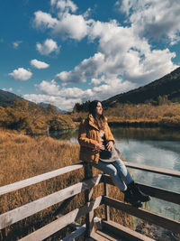 Beautiful young woman wearing autumn clothes, enjoying view of fall scenery by a lake