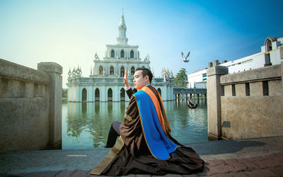 Young man wearing graduation gown while sitting by lake