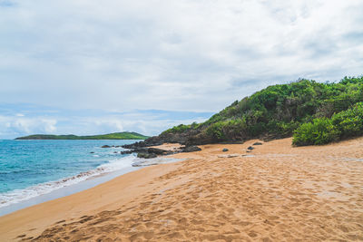 Panoramic view of empty tropical red sand beach and blue water against blue sky and clouds