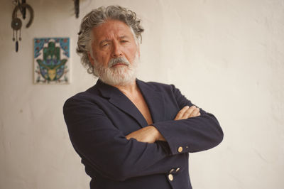 Portrait of senior man with arms crossed standing against wall