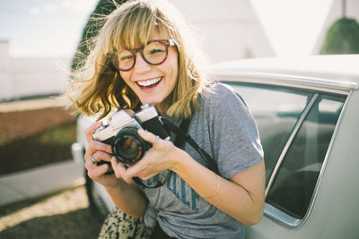 Happy teenager holding camera while standing by car