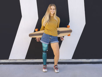 Delighted female skater with bionic prosthesis of leg standing near building in street and looking at camera