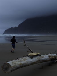 Man standing on rock by sea against sky