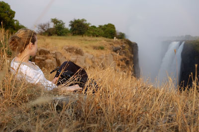 A woman sitting in a grass looking at the victoria's waterfalls in zimbabwe.