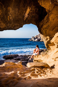 Side view of woman sitting on rock by sea against sky