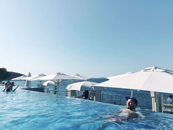 Man relaxing in infinity pool against clear sky