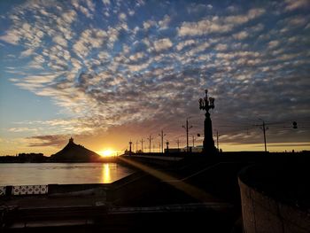 Silhouette bridge by building against sky during sunset