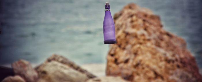 Glass bottle hanging against rocks on sea shore