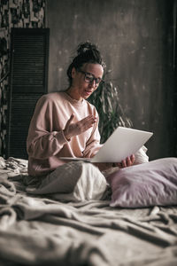 Woman using mobile phone while sitting on bed at home