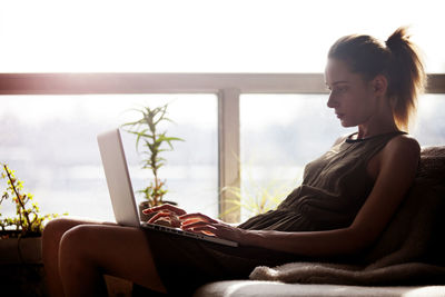 Woman using laptop computer while sitting on sofa at home