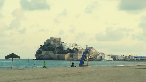 People on beach by buildings against sky