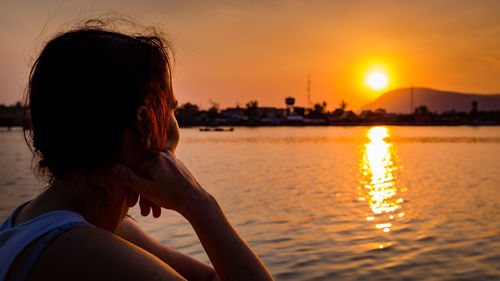 Woman looking at lake against sky during sunset