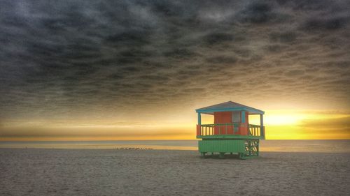 Lifeguard hut on beach against sky during sunset