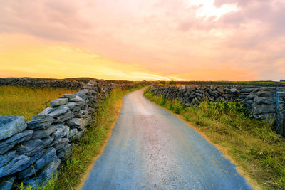 Road amidst field against sky during sunset