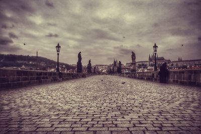 Empty footpath against cloudy sky