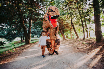 Boy walking with person wearing dinosaur costume in park