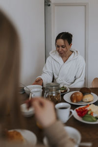 Woman in dressing gown sitting at table and eating breakfast