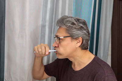Adult gray-haired man brushes his teeth with a toothbrush in the bathroom