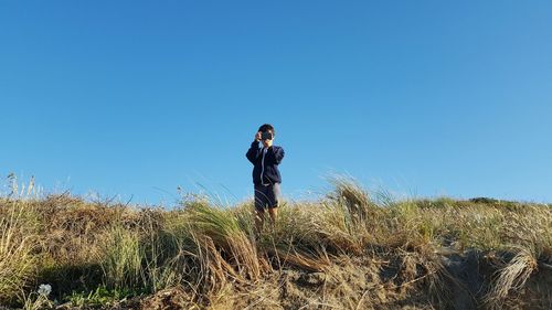 Low angle view of boy photographing with mobile phone against blue sky