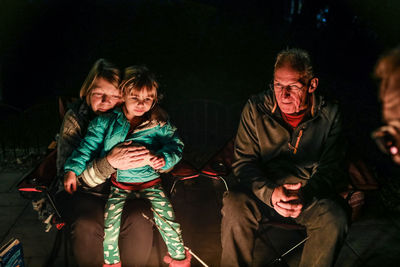 Grandmother hugging grandchild sitting around firepit outside