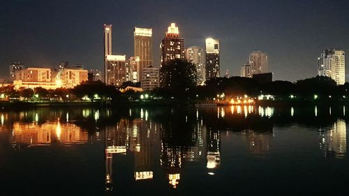 Illuminated buildings by river against sky at night
