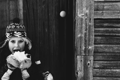 Portrait of girl eating snow against wooden cabin