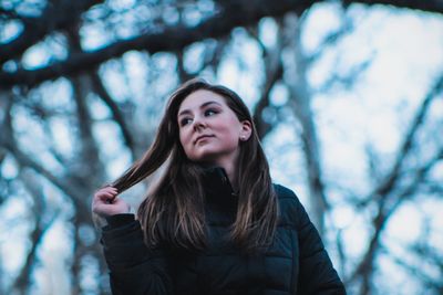 Low angle view of young woman standing against trees