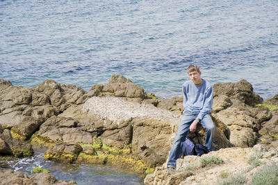 Portrait of young man sitting on rocks against lake