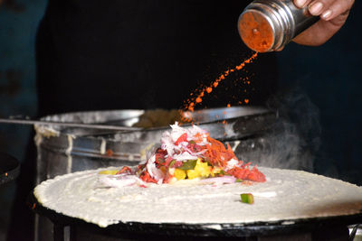 Midsection of man putting spice on dosa