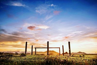Wooden posts on land against dramatic sky during sunset