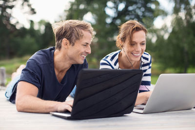 Happy mature couple using laptops while lying on pier