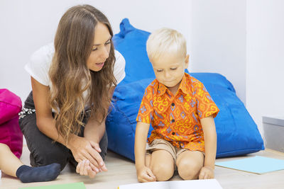 Mid adult teacher teaching student while sitting on floor against bean bag at school