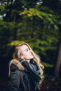 Young woman looking away while standing in forest