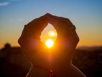 Close-up of woman hand against sun during sunset