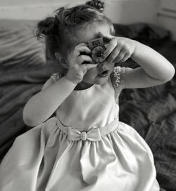 High angle portrait of cute girl photographing with toy camera on bed