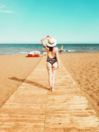 Full length rear view of seductive woman wearing one piece swimsuit standing at beach