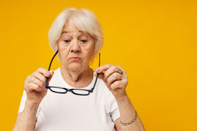 Portrait of young woman holding thermometer against yellow background