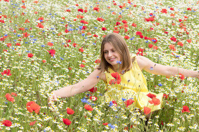 A beautiful young blonde woman in a yellow dress stands among a flowering field