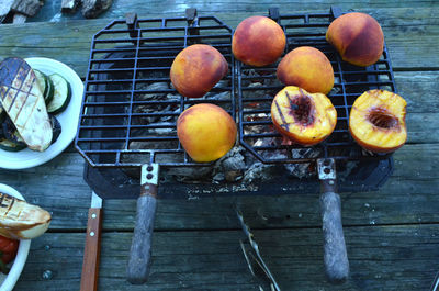 Peach halves grilling on top of a small tabletop hibachi grill on picnic table outdoors