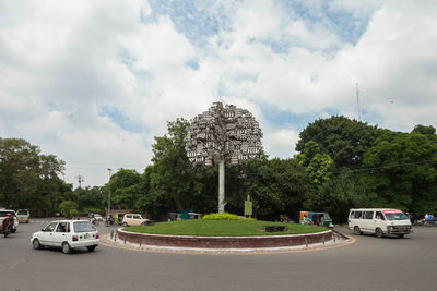 Cars on road by trees against sky