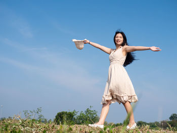 Woman with arms raised on field against sky