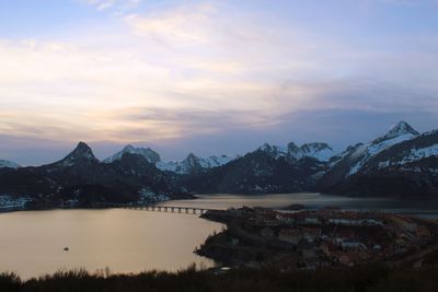 Scenic view of lake by snowcapped mountains against sky during sunset