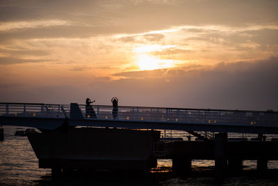 Silhouette people on bench by sea against sky during sunset