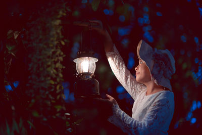 Side view of young woman holding illuminated lighting equipment