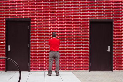 Rear view of man standing against brick wall with closed doors