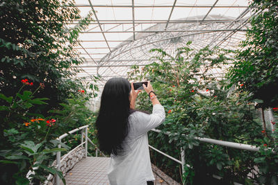 Side view of woman photographing against plants