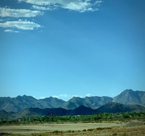 Scenic view of field and mountains against blue sky