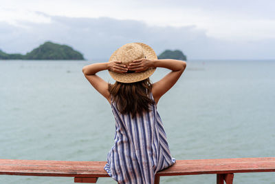 Rear view of woman standing by sea against sky