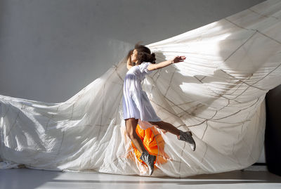 Full length of teenager girl jumping against curtain